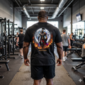 Oversized vintage black t-shirt featuring a small front chest oval skull logo and a massive high-contrast back print of a muscular gladiator Spartacus standing defiant, surrounded by roaring flames and gritty ink-wash textures with bold Apocalypse Gym Wear branding.