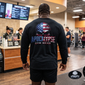 Apocalypse Gym Wear American Flag Skull long sleeve black gym shirt worn by a bodybuilder. Back view showing cracked distressed patriotic skull graphic with 3D block typography.