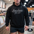 Apocalypse Gym Wear front logo black heavyweight hoodie worn by a bodybuilder in a gym. Front view showing dark grey splatter brush brand typography and skull logo across the chest.