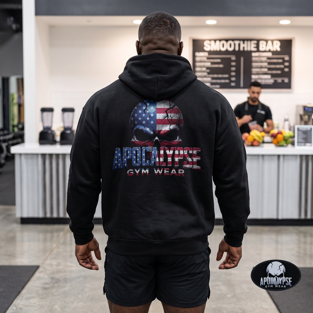 Apocalypse Gym Wear patriotic American flag skull heavyweight black hoodie worn by a bodybuilder in a gym. Back view showing large distressed skull graphic with integrated US flag and 3D textured typography.